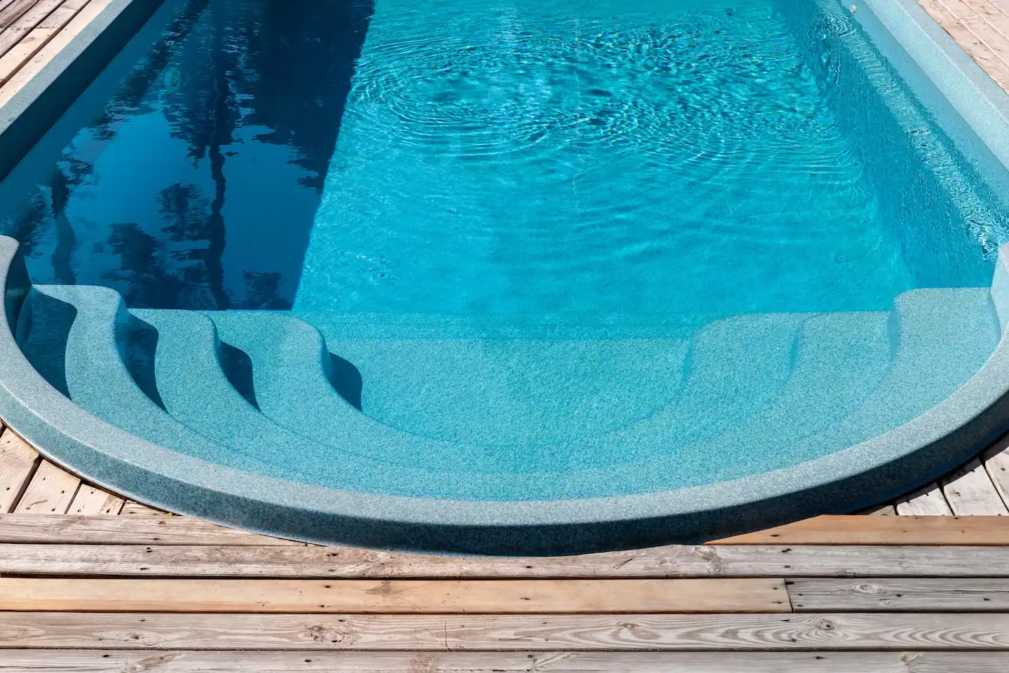 Fiberglass Pool Builder in Austin, TX: Pros, Cons & Cost 2 Fiberglass pool with entrance steps on a wooden deck.
